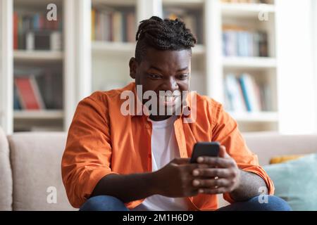 Smiling african american guy using cell phone at home Stock Photo