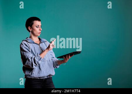 Cheeful woman holding tablet computer using holographic database interface with augmented reality, standing in studio with isolated background. Female having futuristic experience using technology. Stock Photo
