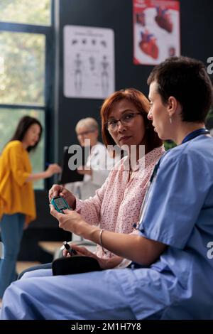 Nurse measuring insulin and glucose level with glucometer, doing checkup examination with diabetic senior asian patient. Using insturment to check blood sample, diabetes consultation. Stock Photo