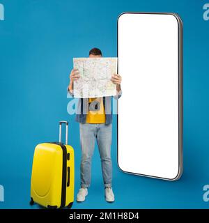 Young male traveler studying map standing by big phone, mockup Stock Photo