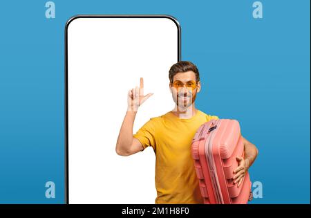 Happy male tourist pointing finger up at smartphone with mockup Stock Photo