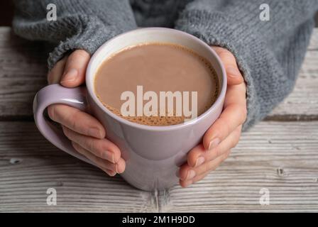 Female hands in a grey sweater holding a mug of hot chocolate on a rustic wooden background Stock Photo