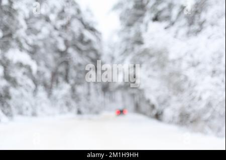 Blurred abstract snow covered trees in forest and red car tail lights on the road Stock Photo