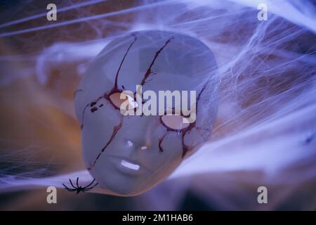 Color image of a white mask, painted with blood, in some spiderwebs and a spider, as Halloween decorations. Stock Photo