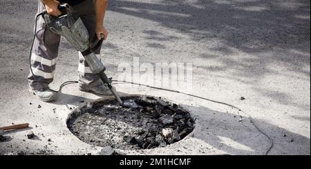 jackhammer in hands of asphalt worker logging underground Stock Photo