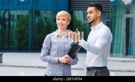 Multiracial couple business colleagues two architects spaniard man and caucasian woman holding folder in hands standing outdoors talking discussing Stock Photo