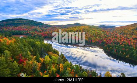 Aerial over stunning pond reflection blue sky and clouds and surrounded by mountains of fall foliage in morning light Stock Photo