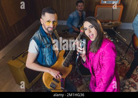 High angle shot of two stylish band members looking at camera. Excited singer and laid-back guitarist. Drummer in the background. . High quality photo Stock Photo