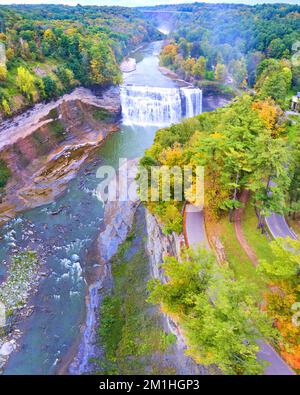 Aerial over raging river with waterfall carving into cliffs covered ...