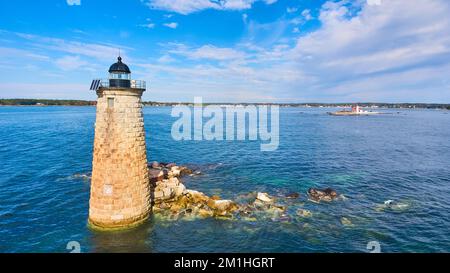 Lone stone tower lighthouse on broken rocks in Maine ocean Stock Photo