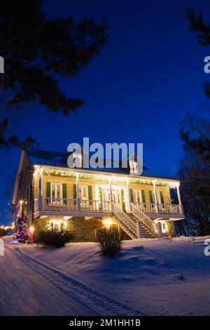 Old 1870 Canadiana cottage style home illuminated with Christmas lights at night in winter. Stock Photo