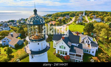 Up close aerial at top of white lighthouse with homes and ocean view in Maine Stock Photo