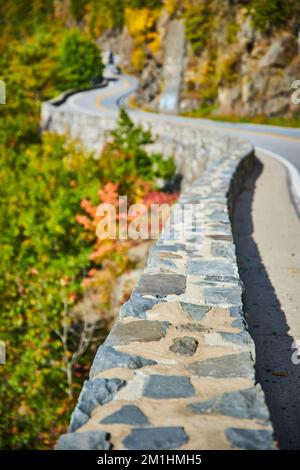 Beautiful stone wall winding along road that zig zags through mountain cliffs into distance Stock Photo