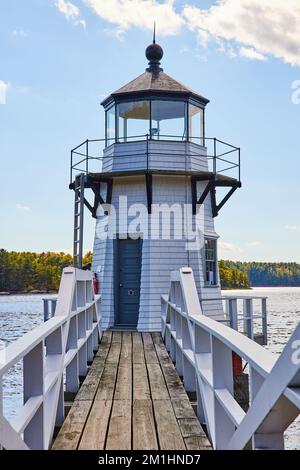 Boardwalk with railing leads to small white lighthouse on Maine river Stock Photo