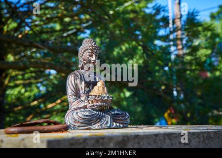 Small Buddhist statue on top of cement column in forest Stock Photo