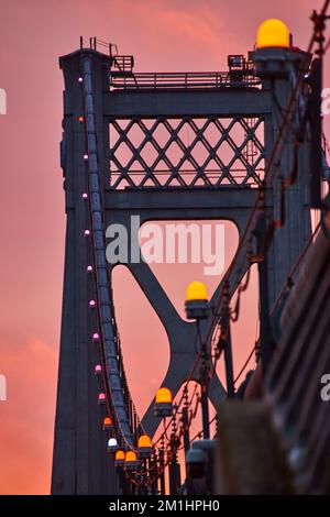 Orange lights in detail on support wires of American bridge with golden light behind Stock Photo