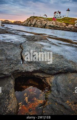 Rocky coast with stunning Maine lighthouse in background during dawn light Stock Photo