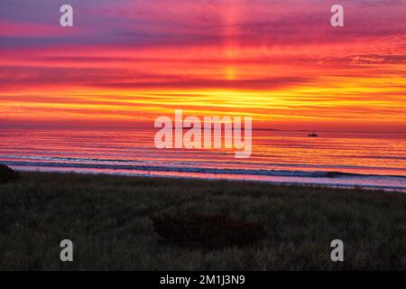 Golden light of sunrise on east coast beach with waves crashing and fishing ship in distance Stock Photo