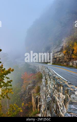 Foggy morning on road through cliffs next to stone block wall Stock Photo