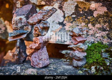 Trio of small cairn stone stacks resting on lichen-covered rocks by wall Stock Photo
