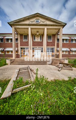 Old abandoned building exterior with stone pillars and brick with overgrown fields Stock Photo