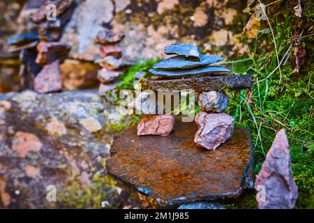 Small stone rocks stacked cairn in beautiful shape against lichen covered rocks and moss Stock Photo