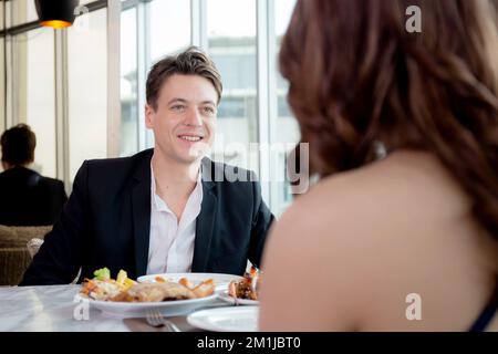 Happy young couple sitting and conversation together in anniversary at restaurant for celebration, man and woman dining while date with romance and re Stock Photo
