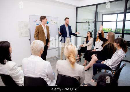 Young caucasian businessman asking opinion and brainstorm of employee while raise hand up for participation together at office, community of business Stock Photo