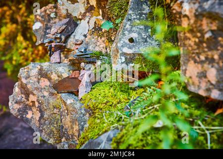 Stone wall at angle with cairn stone stack piles tiny in background and mossy patches Stock Photo