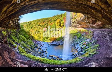 Panoramic view behind waterfall in rocky cavern cliffs with fall foliage mountains in background Stock Photo