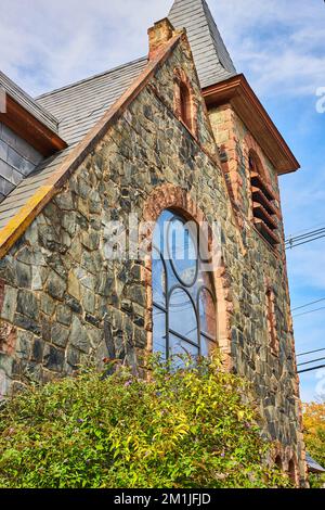 Looking up side of stone church in small town with glass window and simple steeple Stock Photo