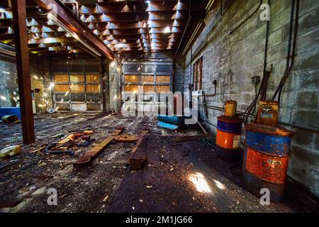 Messy abandoned interior of mechanic shop with garage doors and rusted barrels Stock Photo