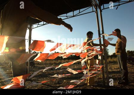 Men setting up lines decorated with plastic pieces coloured in red and white--the colours of Indonesian national flag, at a tent during a preparation of a ceremony to release snake-necked turtles, a local endemic freshwater turtle species, on the side of a lake in Maubesi village, Central Rote, Rote Ndao, East Nusa Tenggara, Indonesia. Stock Photo