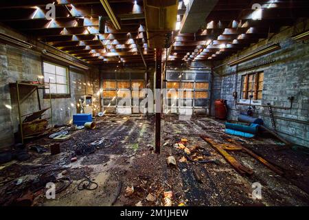 Interior of abandoned double garage mechanic shop with dirty floor and rubble Stock Photo
