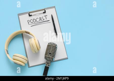 Clipboard with word PODCAST, pen, headphones and microphone on blue background Stock Photo