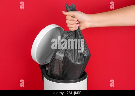 Woman taking garbage bag out of rubbish bin on red background Stock Photo