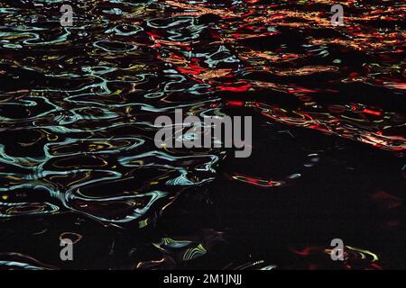 Blue and red lights reflecting off waves of water in river Stock Photo