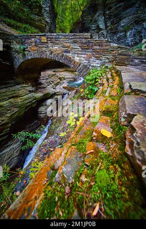 Stunning stone walkway bridge over waterfall gorge with moss and lichen wall Stock Photo