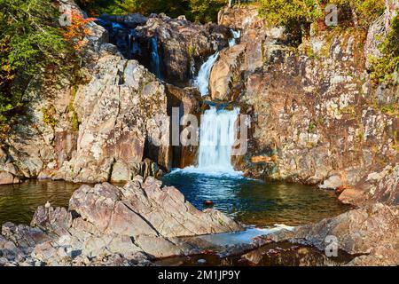Looking up at waterfalls pouring through rocks in forest Stock Photo