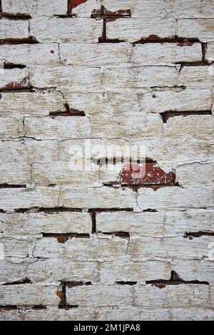 Red brick wall painted white with cracking paint and one exposed red brick Stock Photo