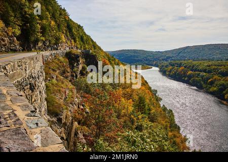 Stone wall and road wind through cliffs and mountains next to Delaware River in early fall Stock Photo