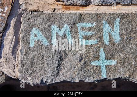 Detail of stone wall graffiti from above Amen and Christian Cross symbol in blue Stock Photo