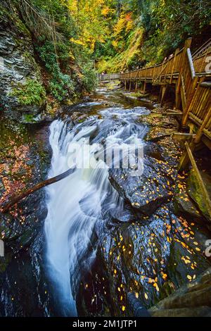 Boardwalk along river with raging falls into abyss and cliffs covered in golden fall leaves Stock Photo