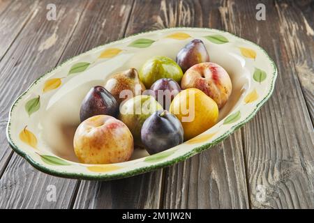 Fresh ripe plums of three colors in plate on wooden background Stock Photo