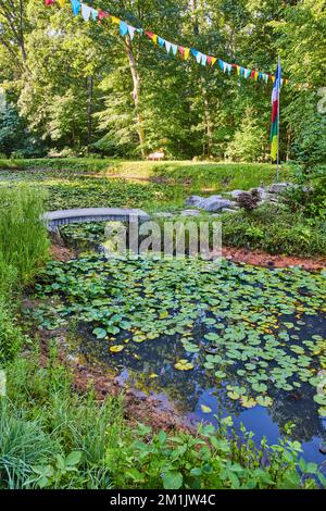 Lily pond in Tibetan Mongolian Buddhist temple with prayer flags and walking bridge to small island Stock Photo
