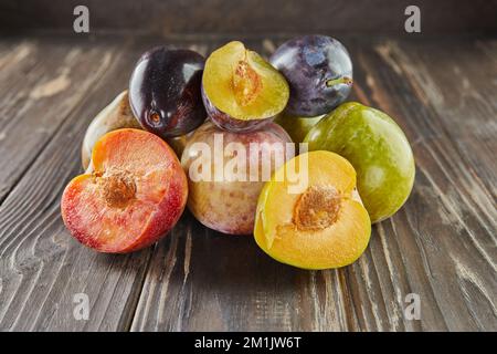 Fresh ripe plums of three colors whole and half on wooden background Stock Photo