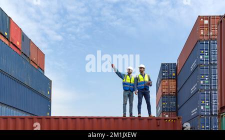 Shipment worker use a walkietalkie to point to container storage location, explain to colleague about planning for next shipment. Young worker with sa Stock Photo