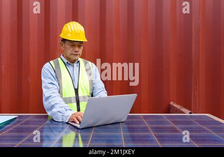 Senior contractor in safety vest and yellow hardhat typing on laptop computer keyboard. Check out the delivery schedule planning for the next shipment Stock Photo