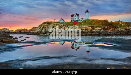 Maine lighthouse reflecting in puddle on rock during golden morning light with overcast clouds Stock Photo