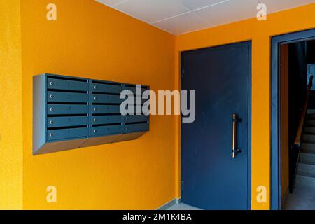 Gray mailboxes on an orange wall in the entrance of an apartment building Stock Photo
